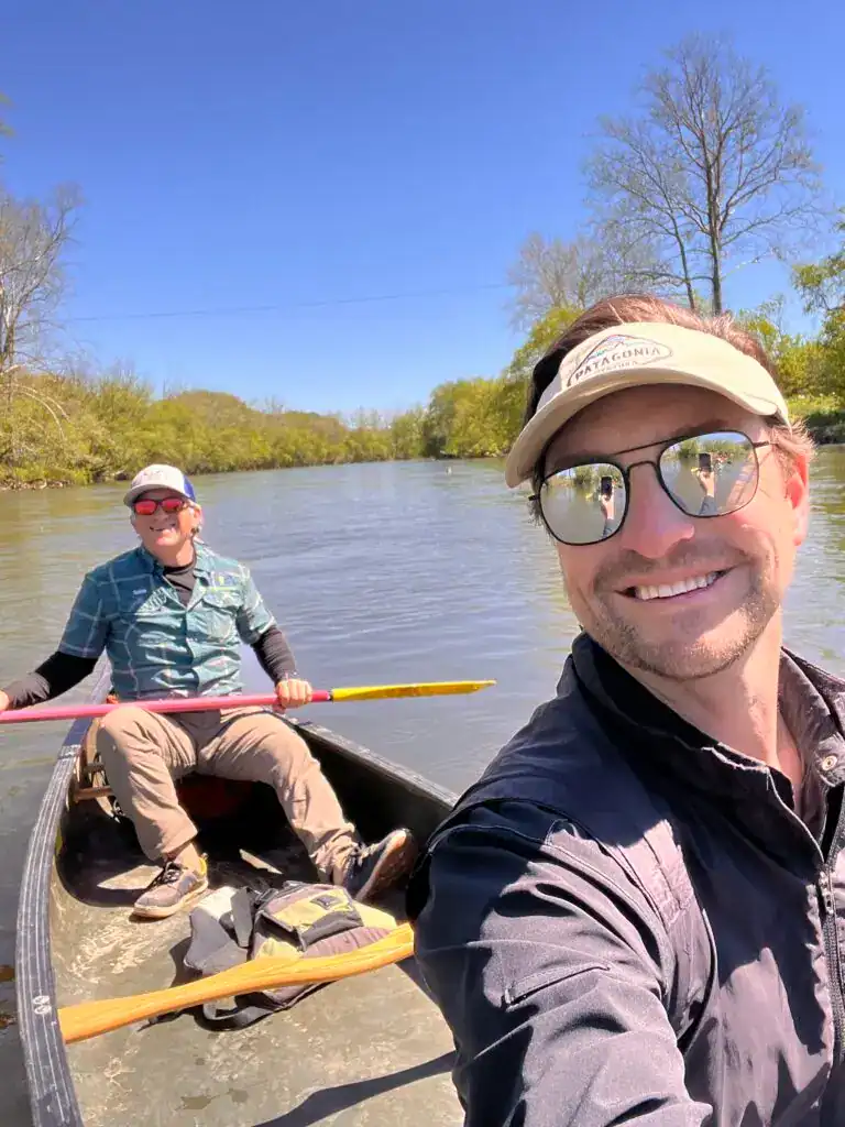 Relaxed outdoor adventure with smiling friends kayaking on scenic river, surrounded by lush greenery.
